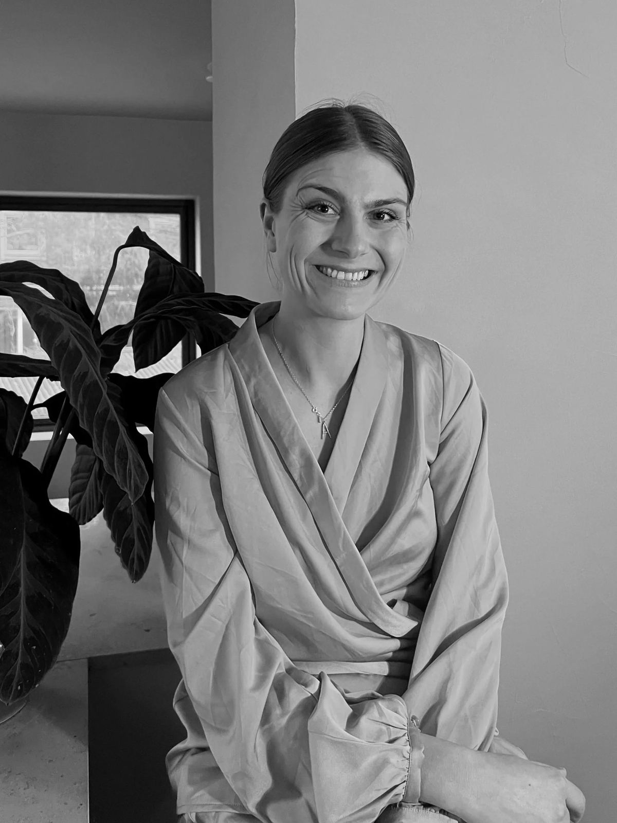 Marie Forsman, grundare av Visselblåsaren, sitter bredvid en växt och ler.